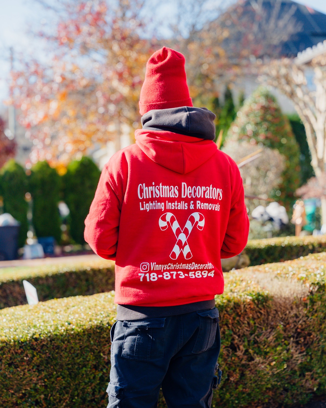 Crew member from behind in a red hoodie printed with The Christmas Decorators and the phone number