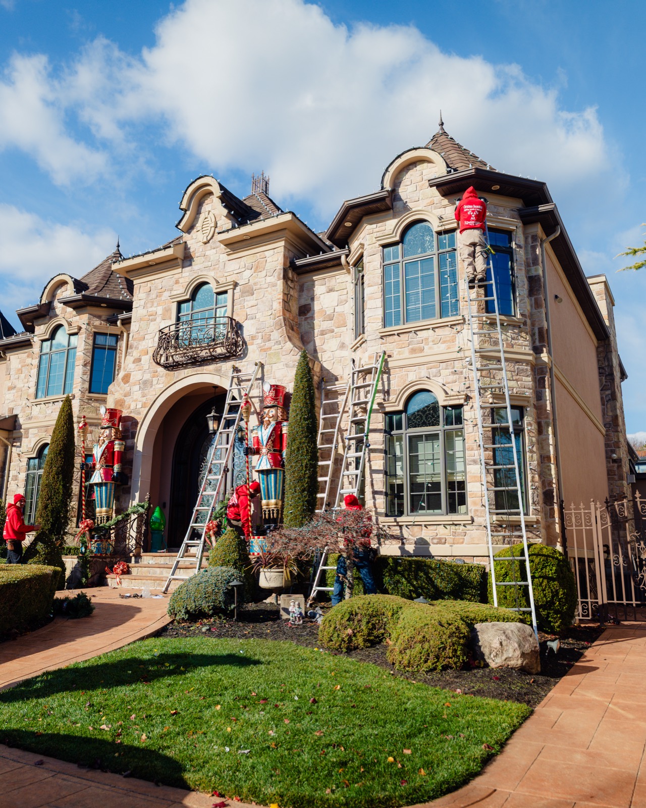 Crew on ladders installing lights on a stone mansion by day