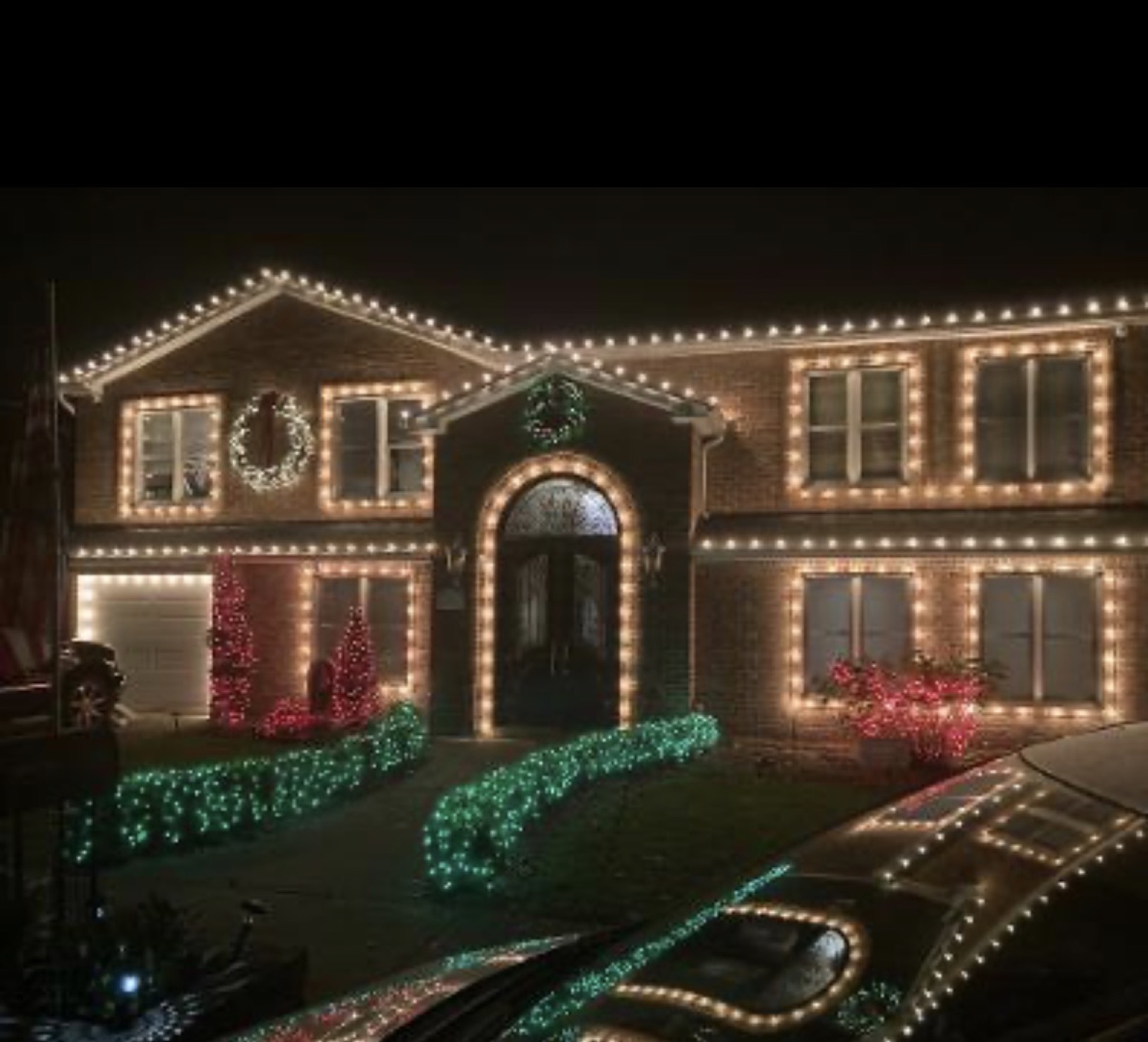 Brick home with outlined windows and green-lit hedges