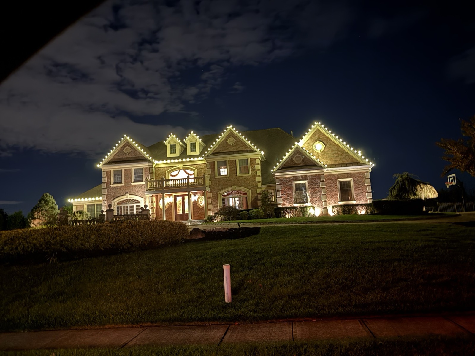 Twin-gabled home with wrapped trees glowing warm white